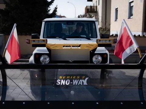 Frontansicht eines Winterdienst-Fahrzeugs mit Schneeschild und rot-weißen Warnfähnchen vor einer Wohnstraße in Regensburg.