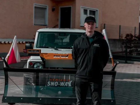 Mitarbeiter in MDZ-Arbeitskleidung vor einem Winterdienst-Fahrzeug mit Schneeschild.