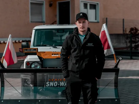 Mitarbeiter mit Cap steht vor dem Schneeschild eines MDZ-Winterdienstfahrzeugs.