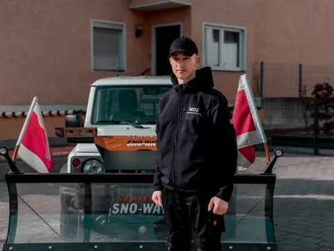 Junger Mitarbeiter in MDZ-Arbeitskleidung vor einem Winterdienstfahrzeug.