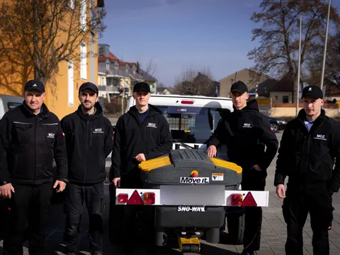 Fünfköpfiges MDZ-Team steht hinter einem Streugutanhänger vor winterlicher Wohnbebauung.