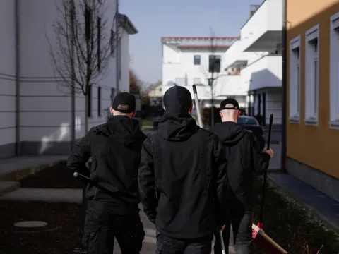 Drei Mitarbeiter gehen mit Besen und Schrubber ausgestattet zwischen Wohnhäusern zur nächsten Reinigungsstelle.