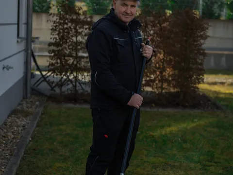 Mitarbeiter posiert mit Laubrechen im gepflegten Garten einer Wohnanlage.