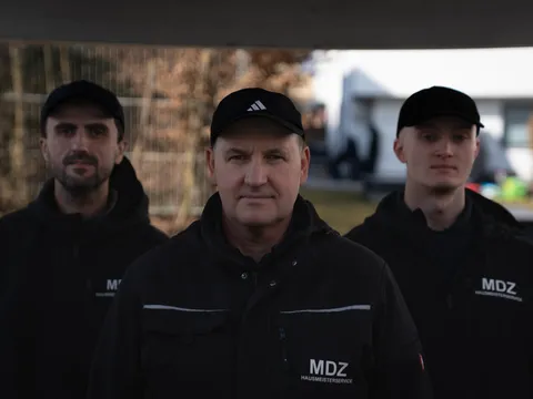 Drei Mitarbeiter stehen dicht beieinander unter einem überdachten Carport-Bereich.