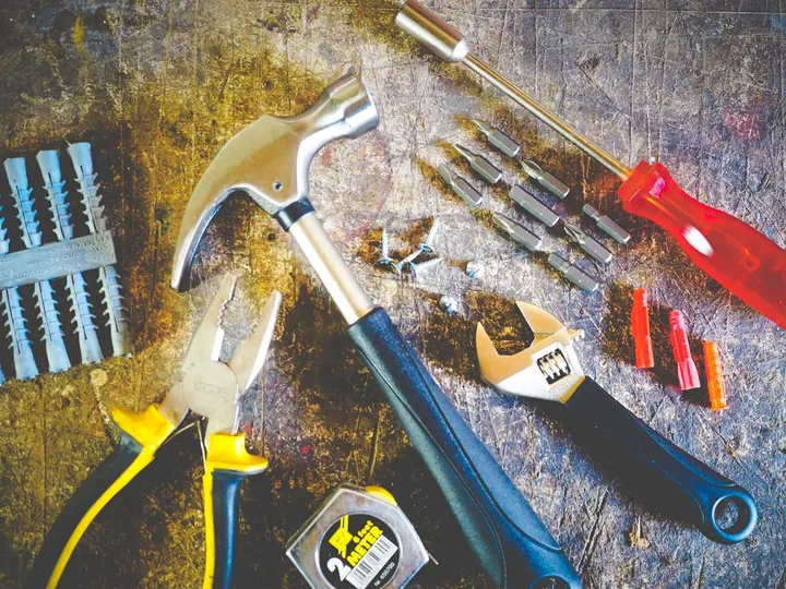 Hammer, Zange, Schraubenschlüssel, Schraubendreher und Dübel liegen auf einer Werkbank bereit.