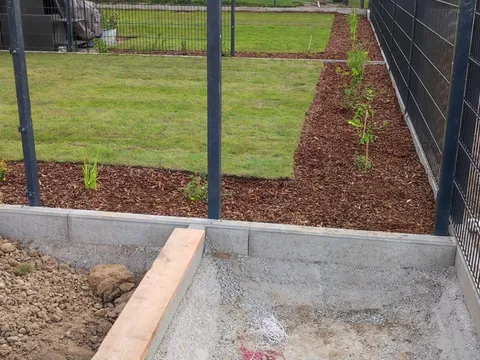 Neu angelegter Rasen mit frisch gemulchten Randbeeten zwischen zwei Wohngebäuden.