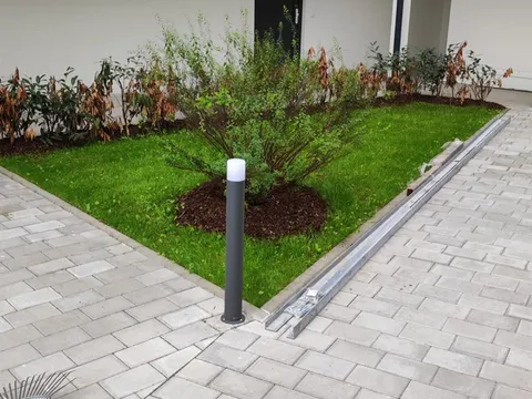 Gepflegter Innenhof mit frisch gemähtem Rasen, gemulchtem Beet und bereitstehendem Rechen.