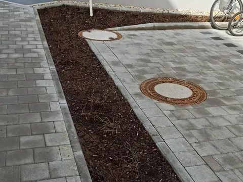 Gereinigter Pflasterbelag mit Schachtdeckeln und frisch gemulchtem Beet.