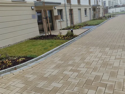 Sauberer Plattenweg mit gepflegtem Rasenstreifen entlang einer Wohnanlage.